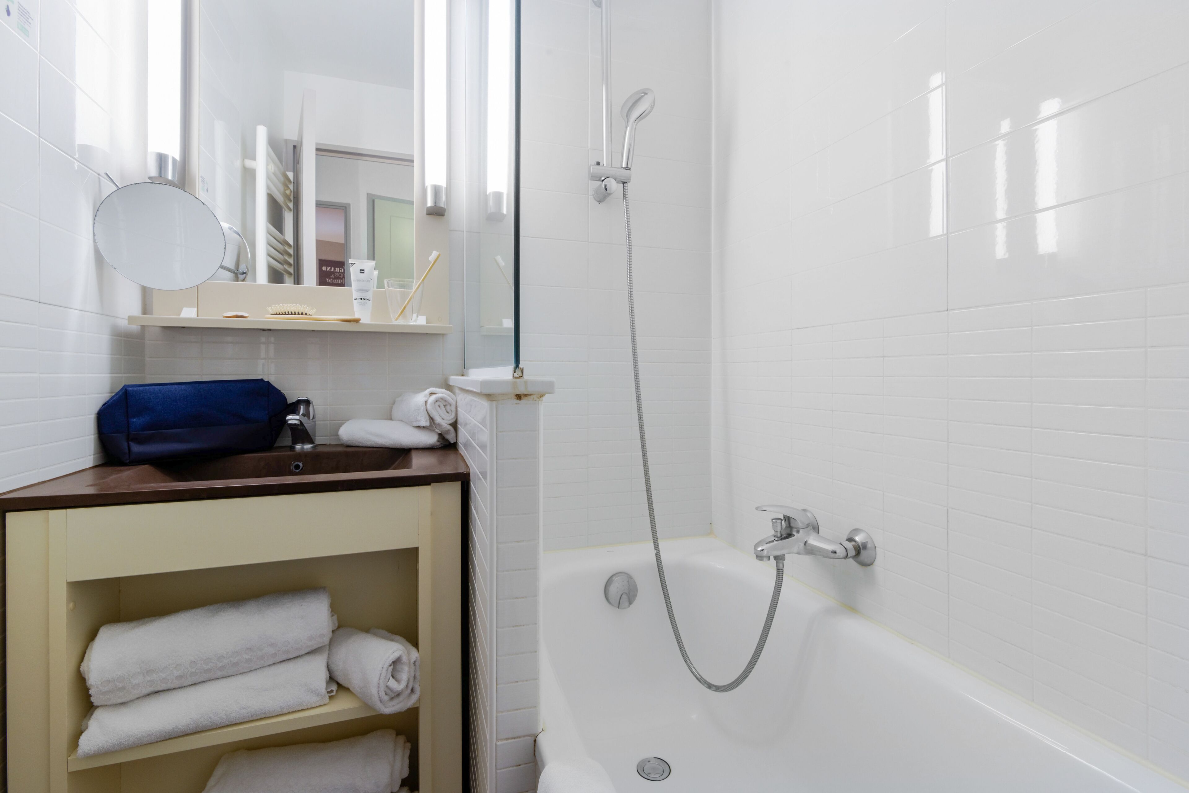 Een badkamer met een wit bad, een douche, een spiegel en een plank met handdoeken.
