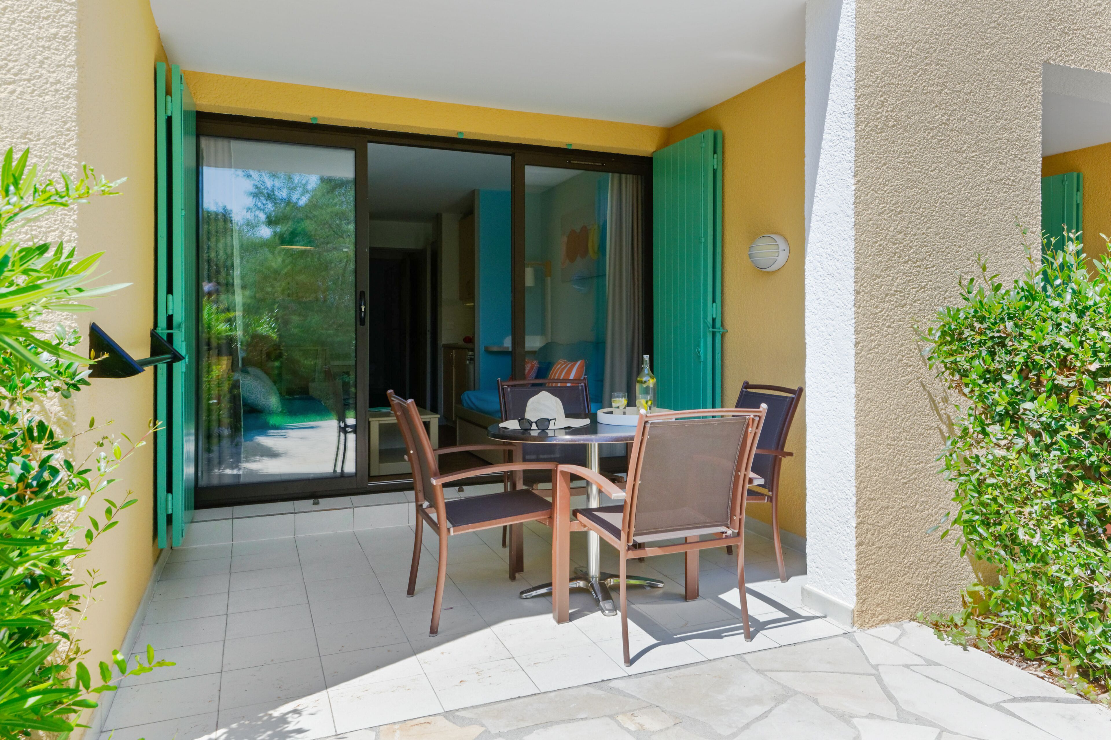 An outdoor patio with a table and chairs, a sliding glass door, and a view of the garden.