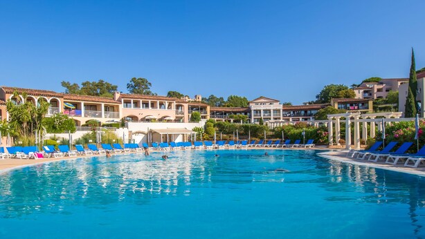 Una piscina grande con sillas reclinables azules y un edificio con varios balcones al fondo.
