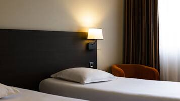 Une chambre d’hôtel avec deux lits, une lampe fixée au mur, une chaise et un rideau.