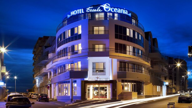 Un hôtel à plusieurs étages, reconnaissable à son enseigne bien visible indiquant « Hôtel Escale Oceania ».