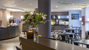 Un hall d’hôtel moderne avec un comptoir d’accueil, un grand vase rempli de fleurs et un espace détente comprenant des tables et des chaises.