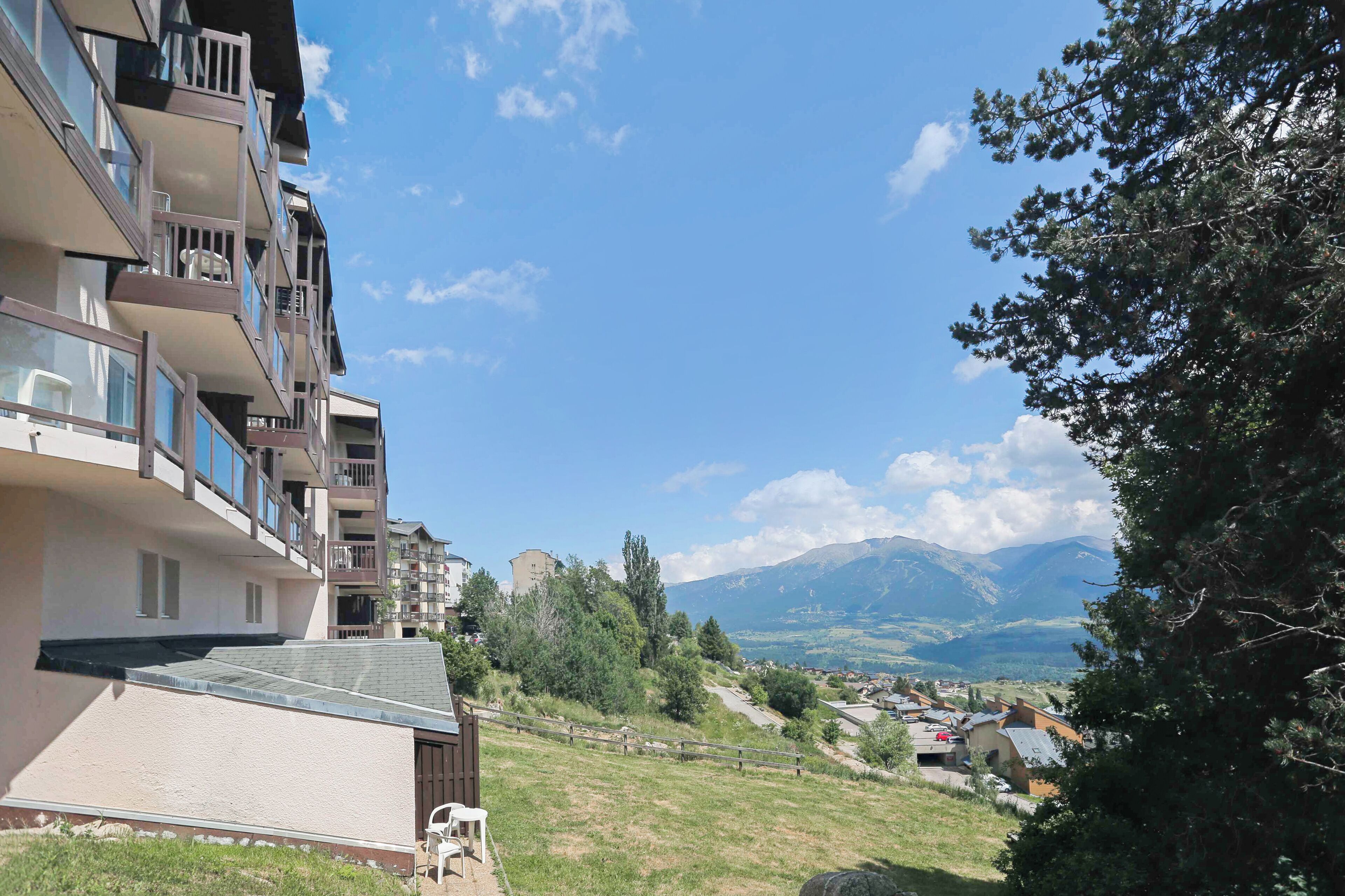 A residential building with balconies, a grassy area, and a mountainous landscape in the background.