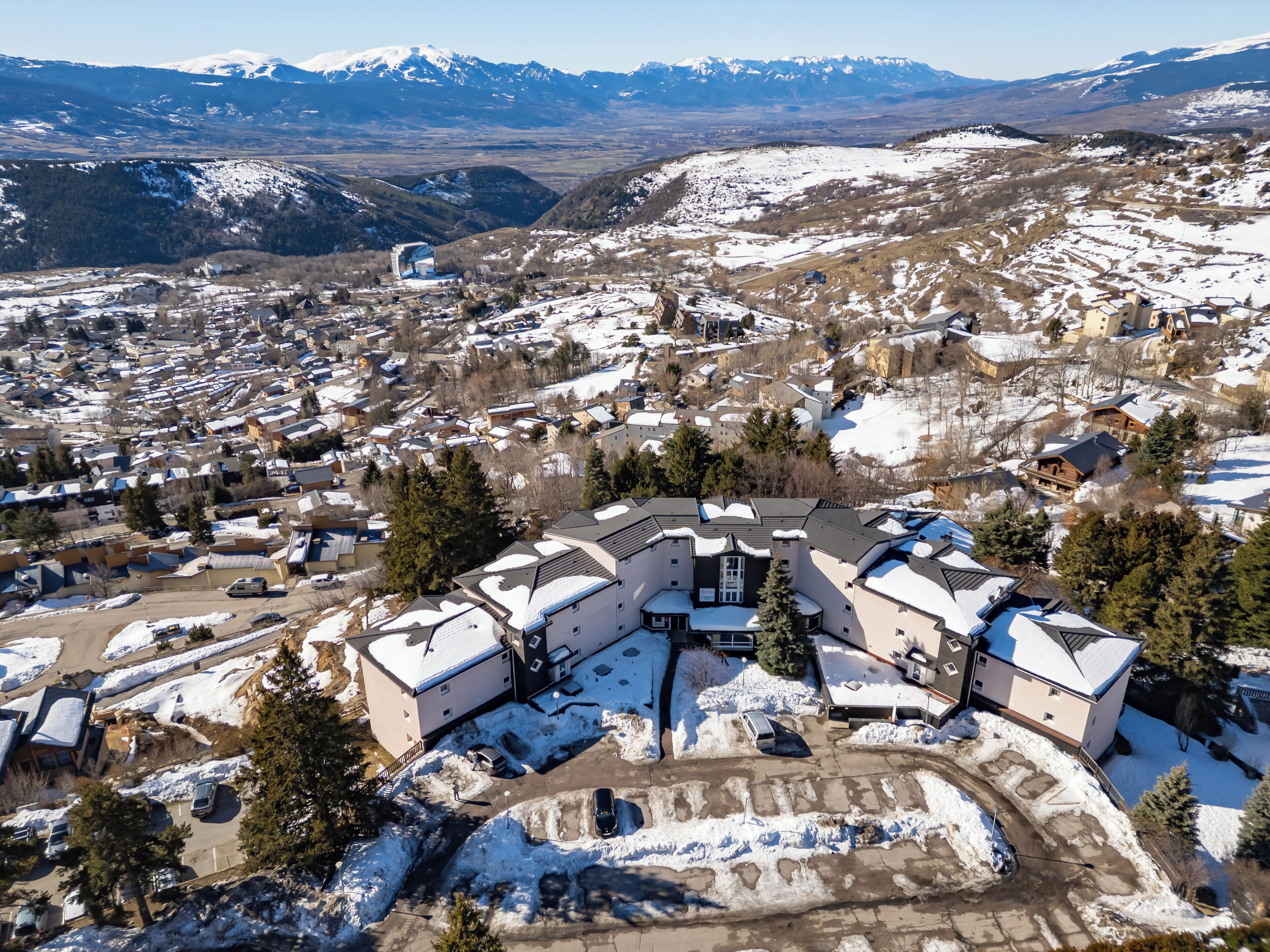 Un grand bâtiment à plusieurs étages, doté d’une cour intérieure, et entouré d’un paysage enneigé et d’arbres.