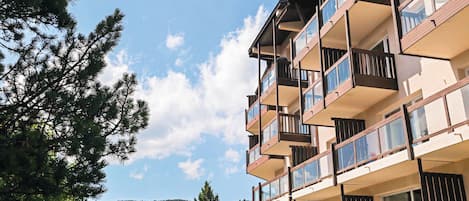 Un edificio de varios pisos con balcones, mobiliario exterior y vistas a árboles y colinas.