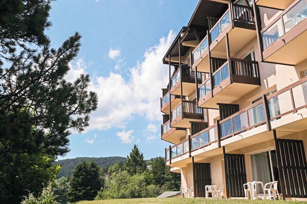 A multi-story building with balconies, outdoor seating, and a view of trees and hills.