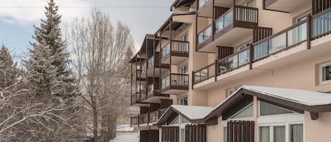 Un edificio de varios pisos con balcones, suelo cubierto de nieve y árboles.