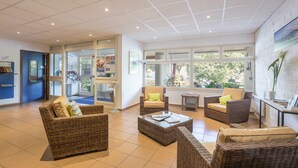 A spacious lobby with wicker furniture, large windows, and a view of the outdoors. - Pierre & Vacances Résidence Eguzki (Saint-Jean-de-Luz)