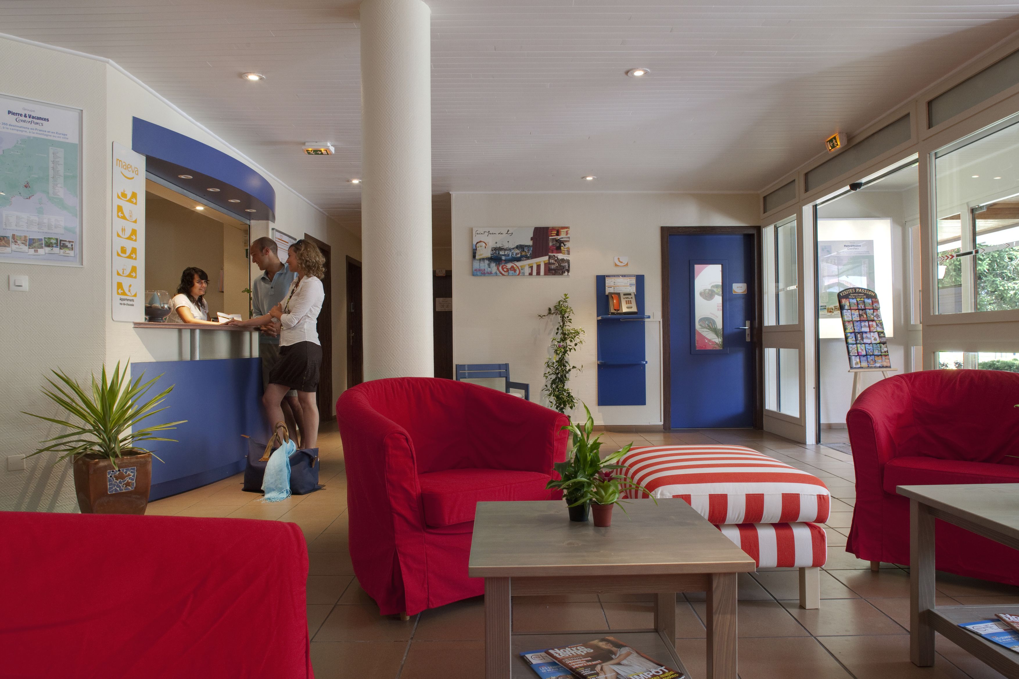 Un espace d’accueil avec un comptoir, des canapés rouges, une petite table et des plantes en pot.