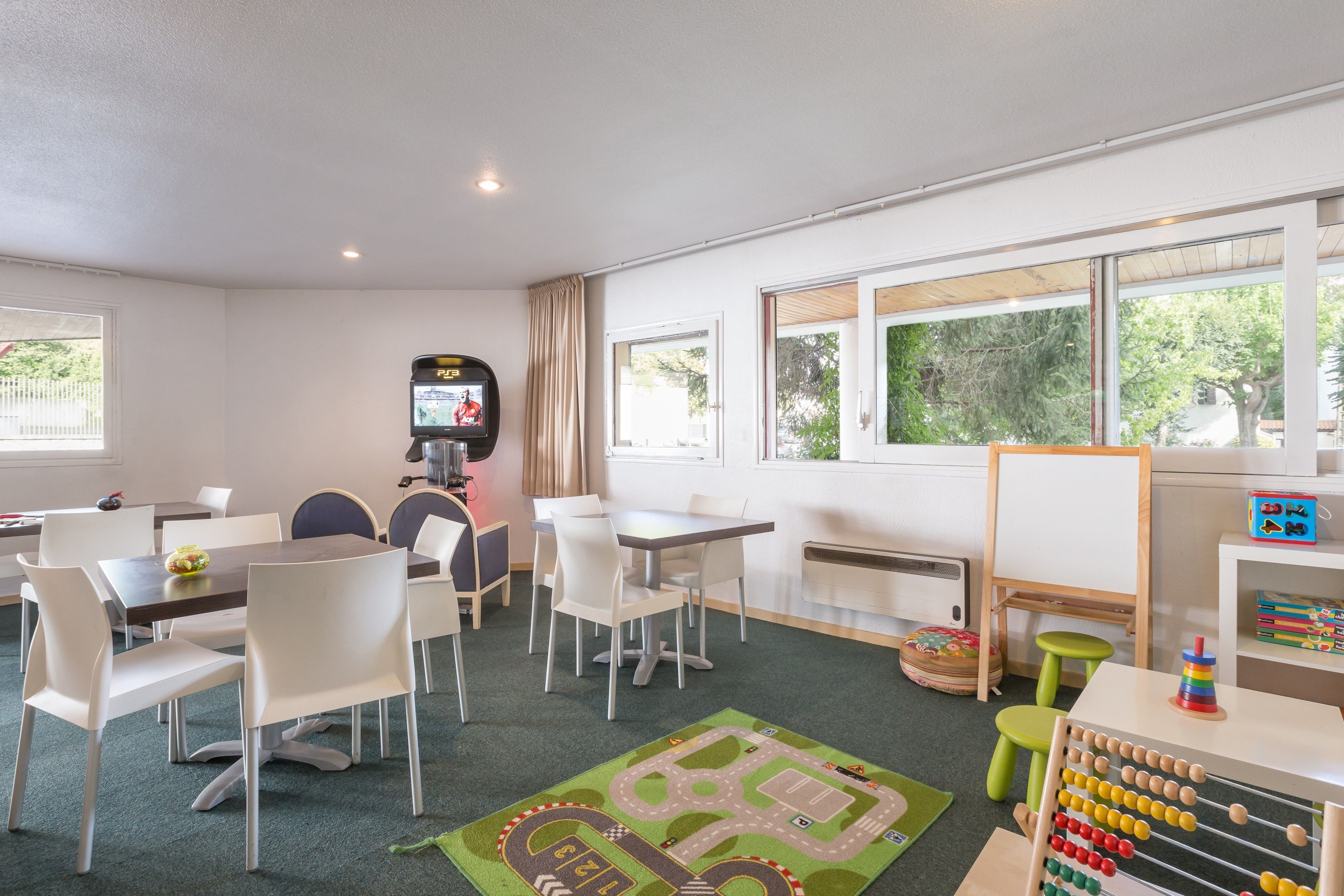 A children's playroom with tables, chairs, a play area, and a large window.