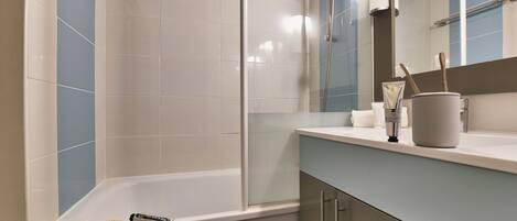 Een moderne badkamer met een douche, een bad en een wastafel met toiletartikelen.