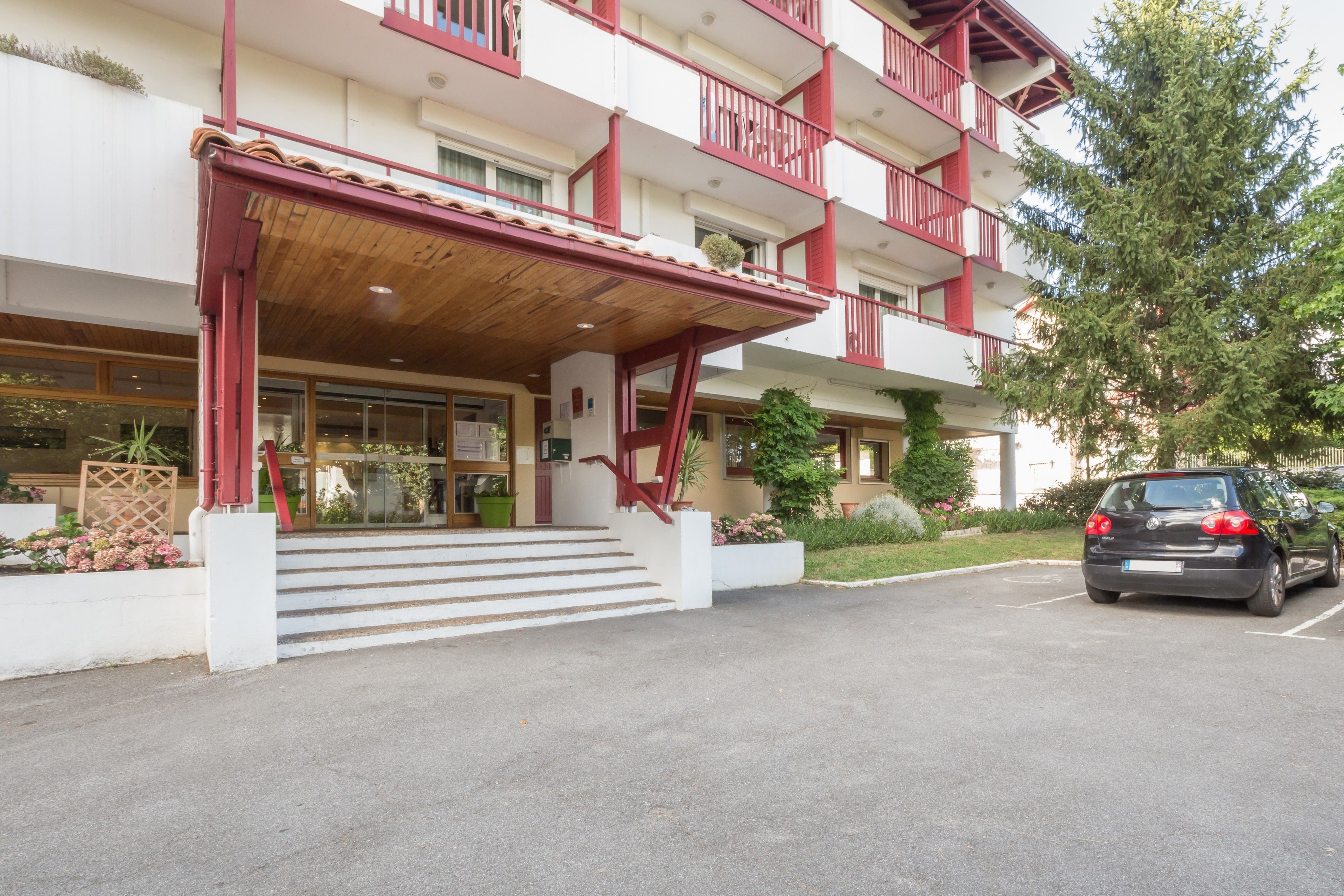 A multi-story hotel with a red and white facade, a covered entrance, and a parking area.