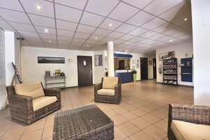 Un vestíbulo con muebles de mimbre, un mostrador de recepción y carteles informativos.