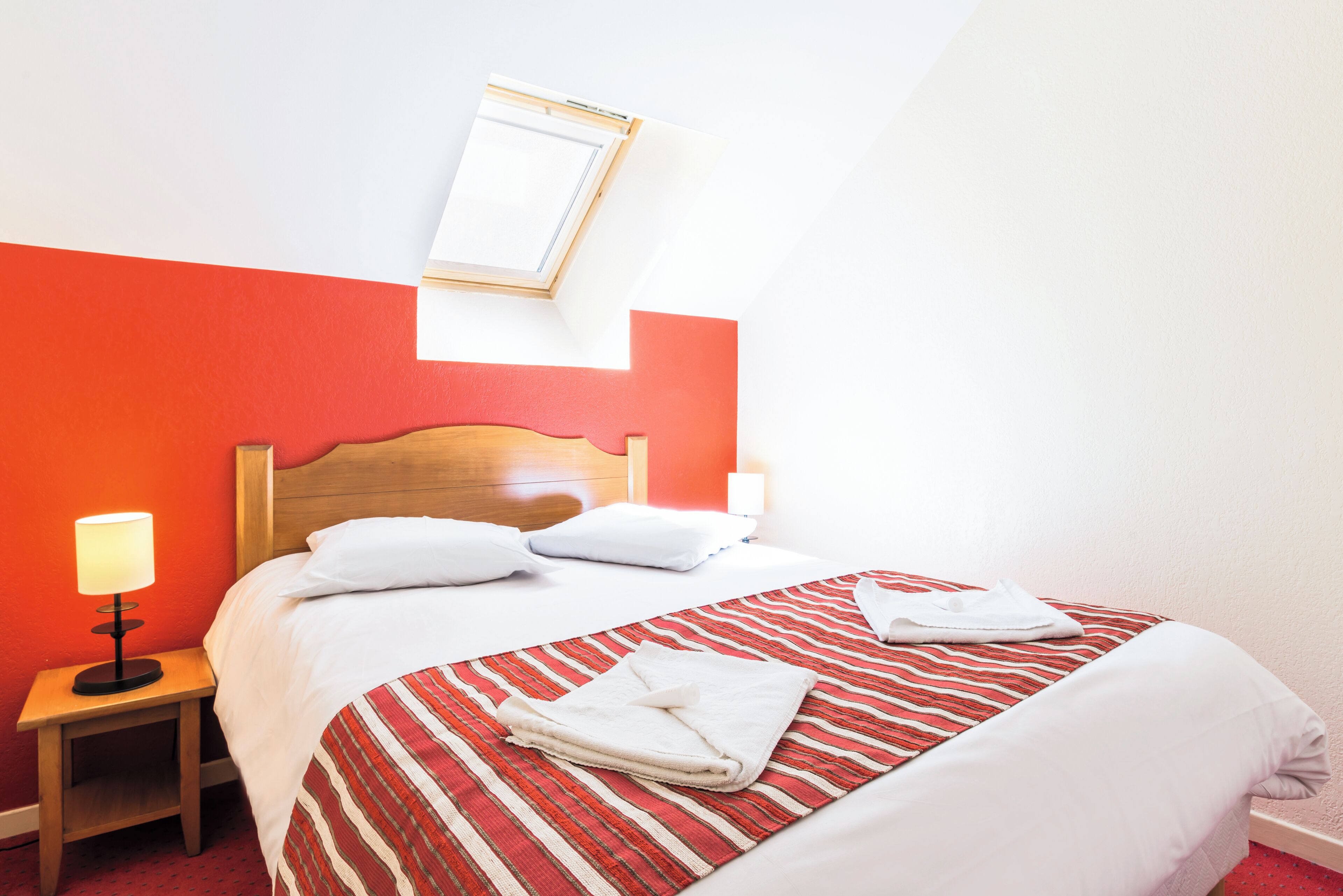 A hotel room with a bed, a nightstand, a lamp, and a mirror on the wall.