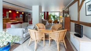 A modern living room with a sofa, wicker chairs, a coffee table, a TV, and a potted plant.