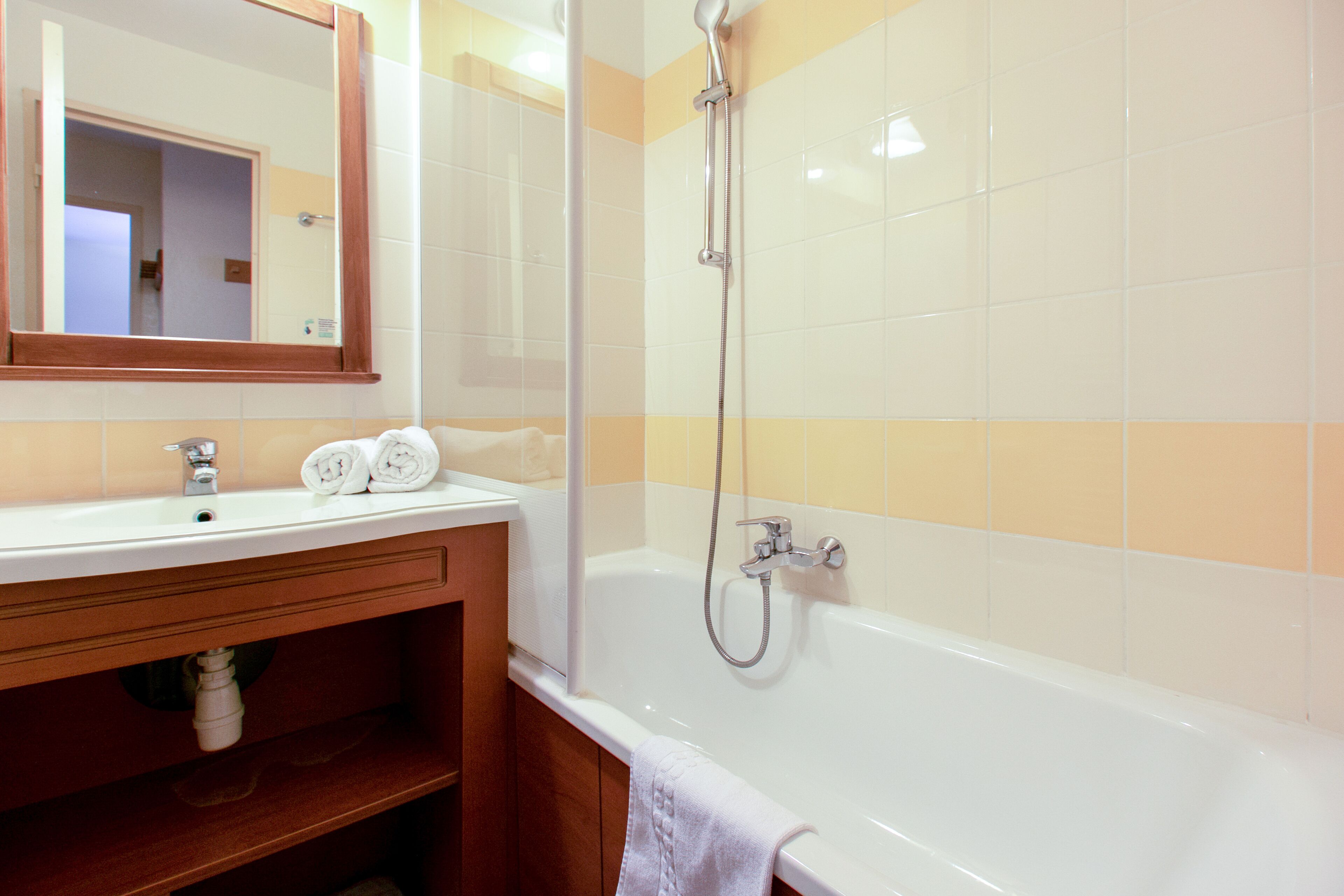 A bathroom with a white bathtub, a wooden vanity, and a mirror.