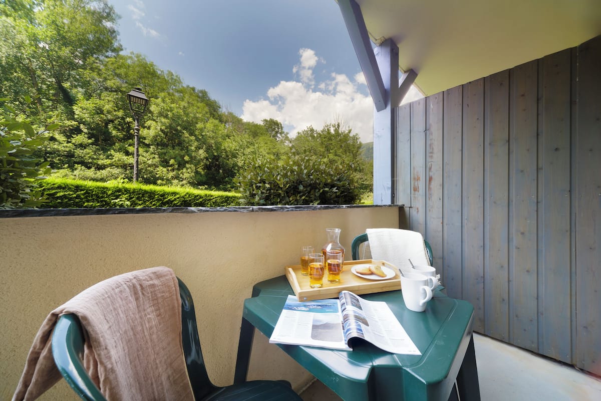 A balcony with a table set for a meal, including a tray with drinks and bread, and a chair with a towel.
