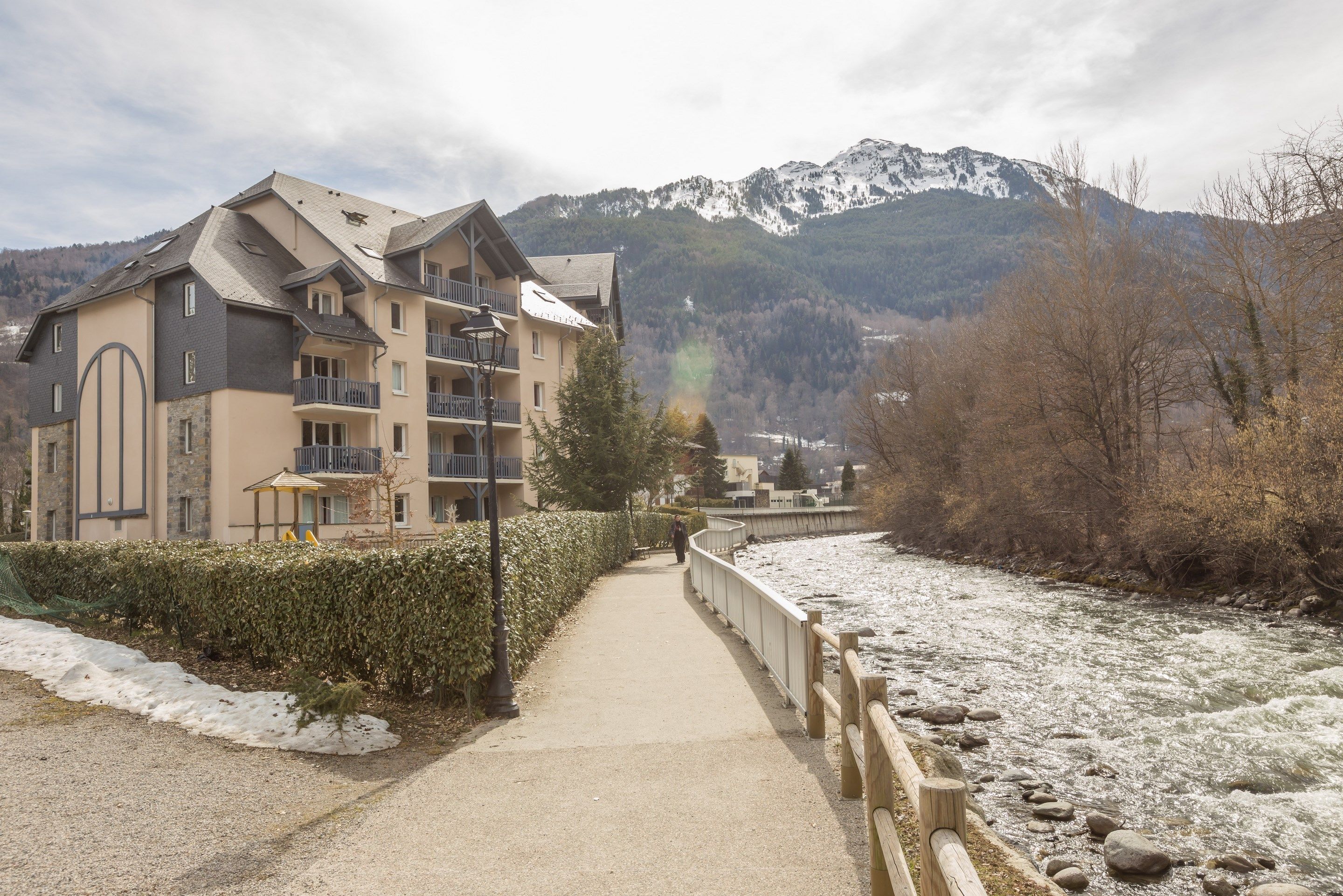 A hotel with a balcony, a view of a river, and mountains in the background.