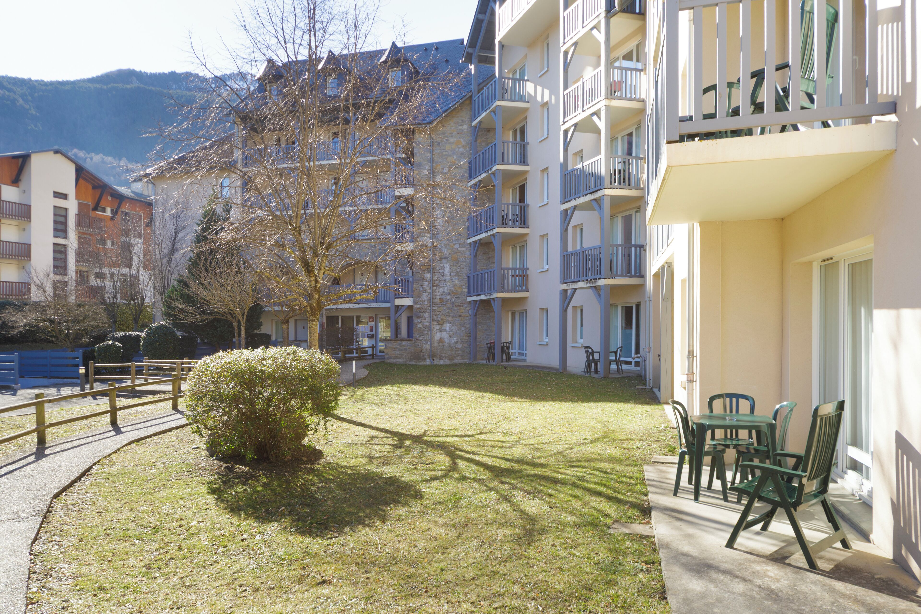 A courtyard with a small lawn, a wooden bench, and outdoor furniture.