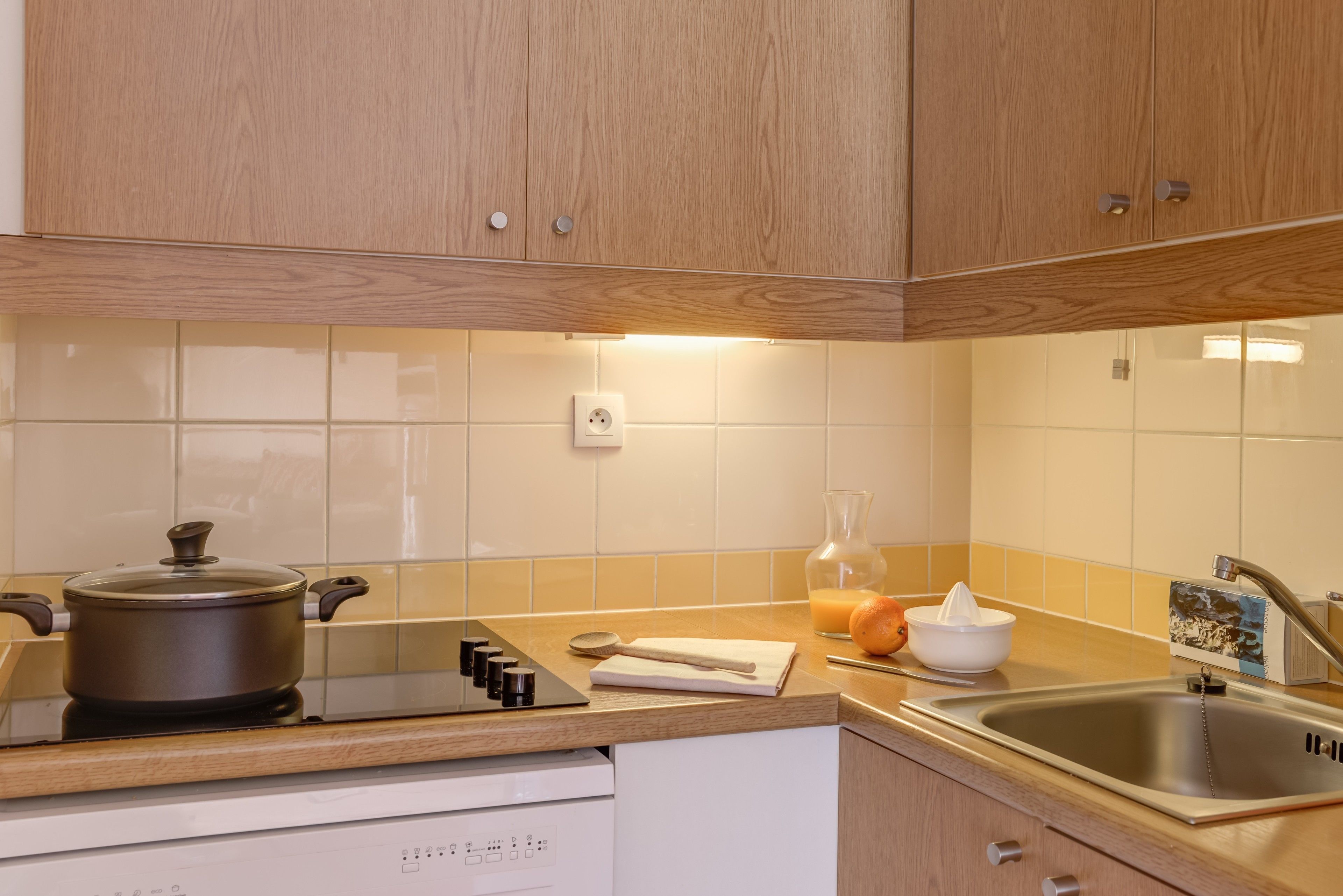 Una cocina con gabinetes de madera, estufa, pileta y salpicadero azulejado.