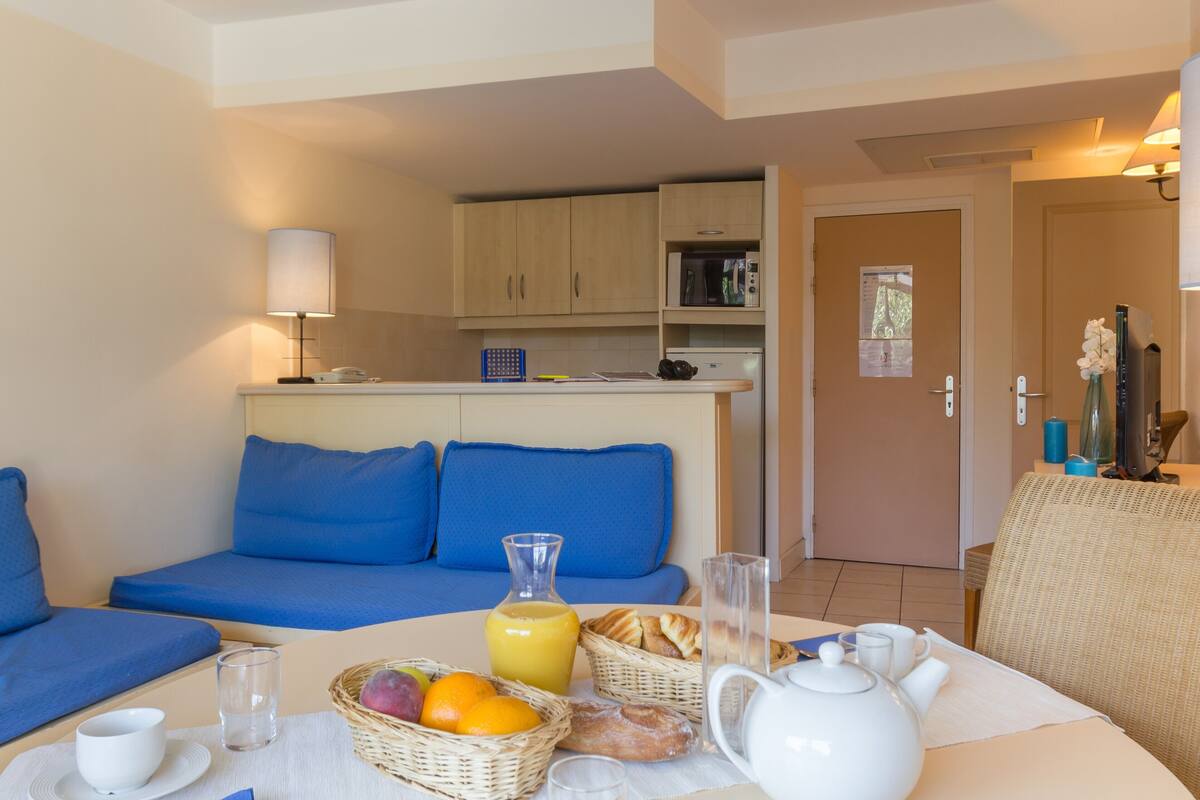 Una camera moderna con un divano blu, un tavolo per la colazione con frutta, un bollitore e un forno a microonde.