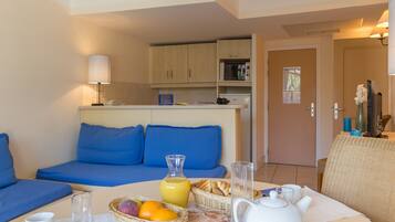 A modern room with a blue sofa, breakfast table with fruit, a kettle, and a microwave.