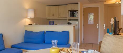 A modern room with a blue sofa, breakfast table with fruit, a kettle, and a microwave.