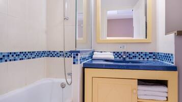 A bathroom with a bathtub, a shower, a sink with a mirror above it, and a cabinet with towels.