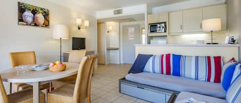 A modern living room with a sofa, dining table, and chairs. There is a kitchen area with cabinets and a microwave.