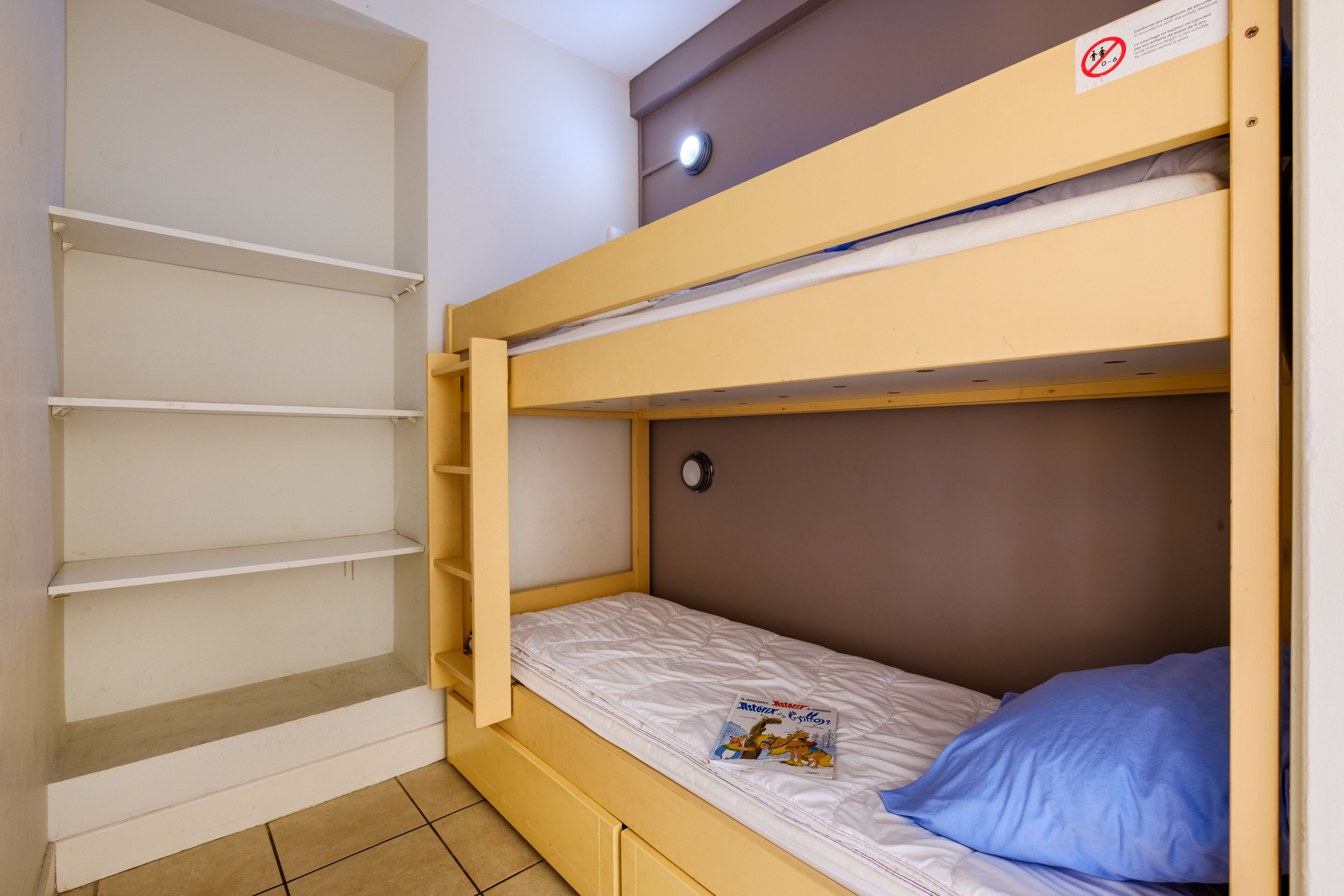 Een stapelbed met een bijbehorende plankkast, een klein horloge en een tijdschrift op het bed.