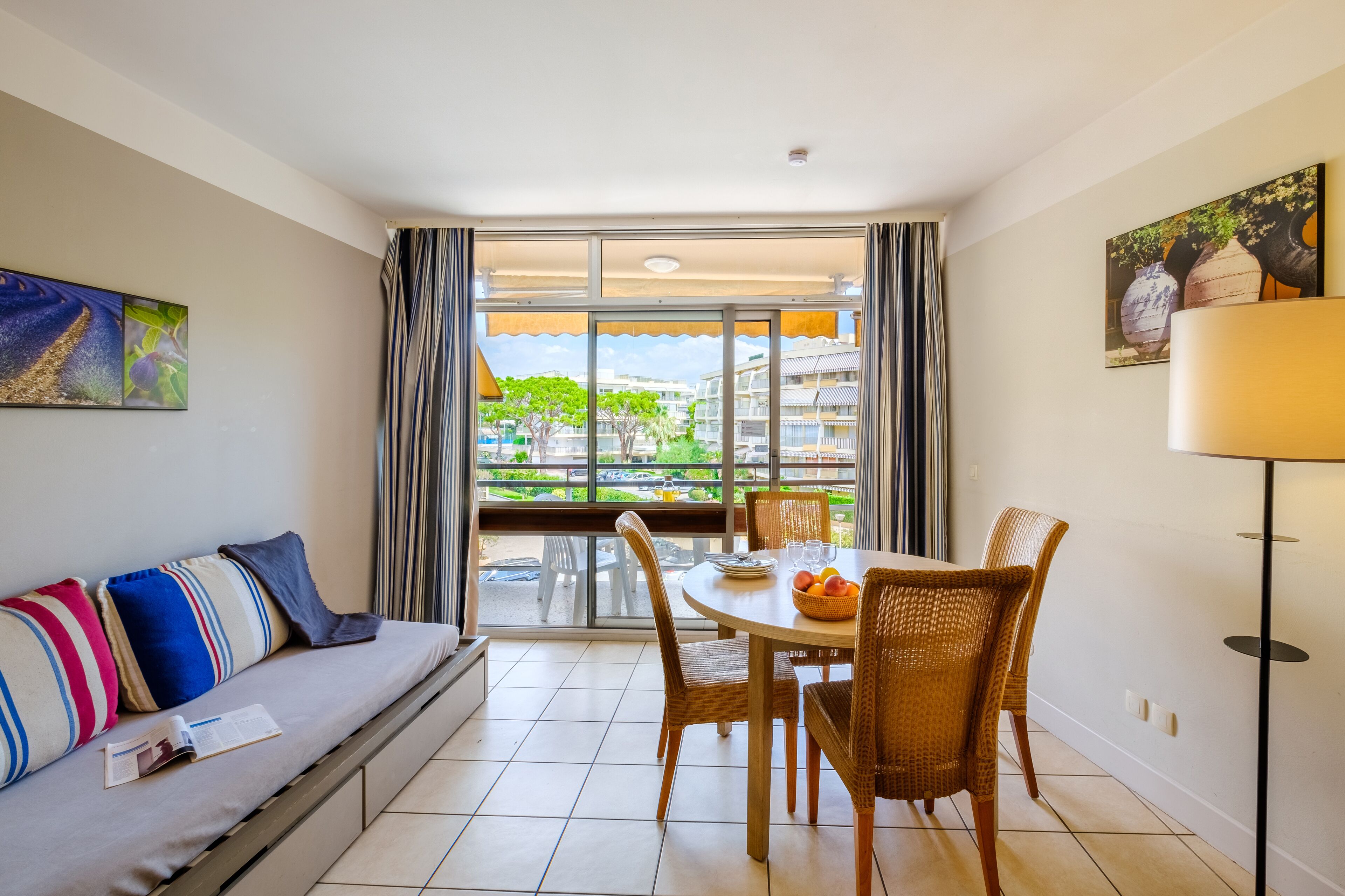 A modern living room with a sofa, dining table, and chairs. A large window offers a view of the outside.