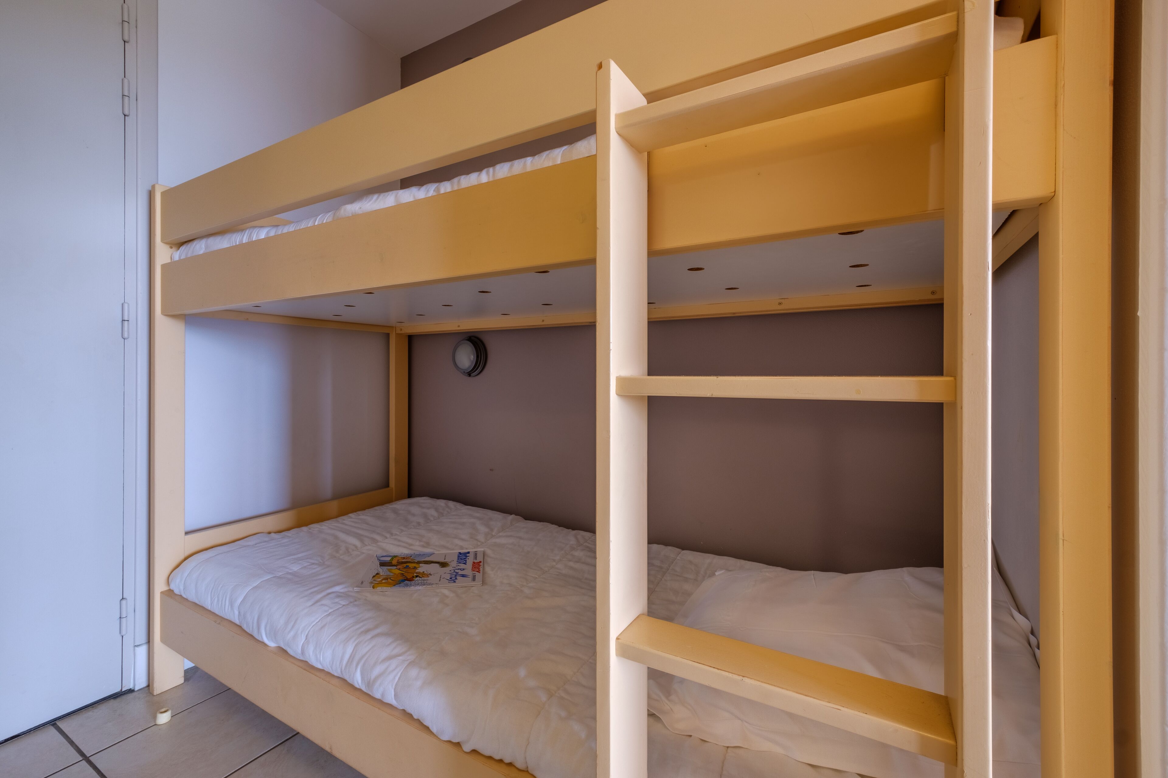 Uma cama beliche com colchão branco e um pequeno relógio na parede.