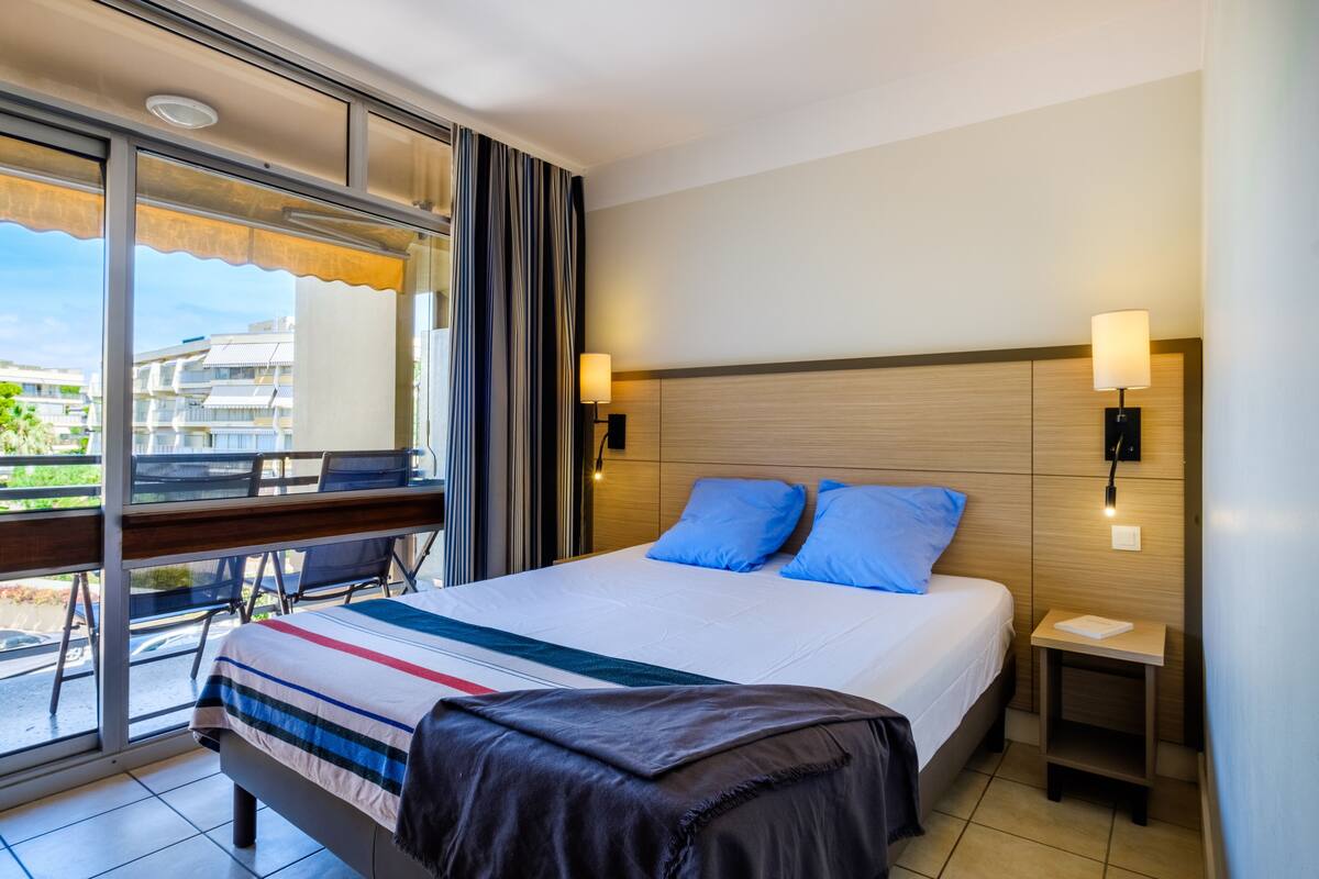 Una camera d'albergo con un letto grande, due cuscini, un comodino con una lampada, una sedia e vista sull'esterno.