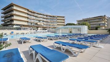 A poolside area with sun loungers and a large building with multiple balconies.
