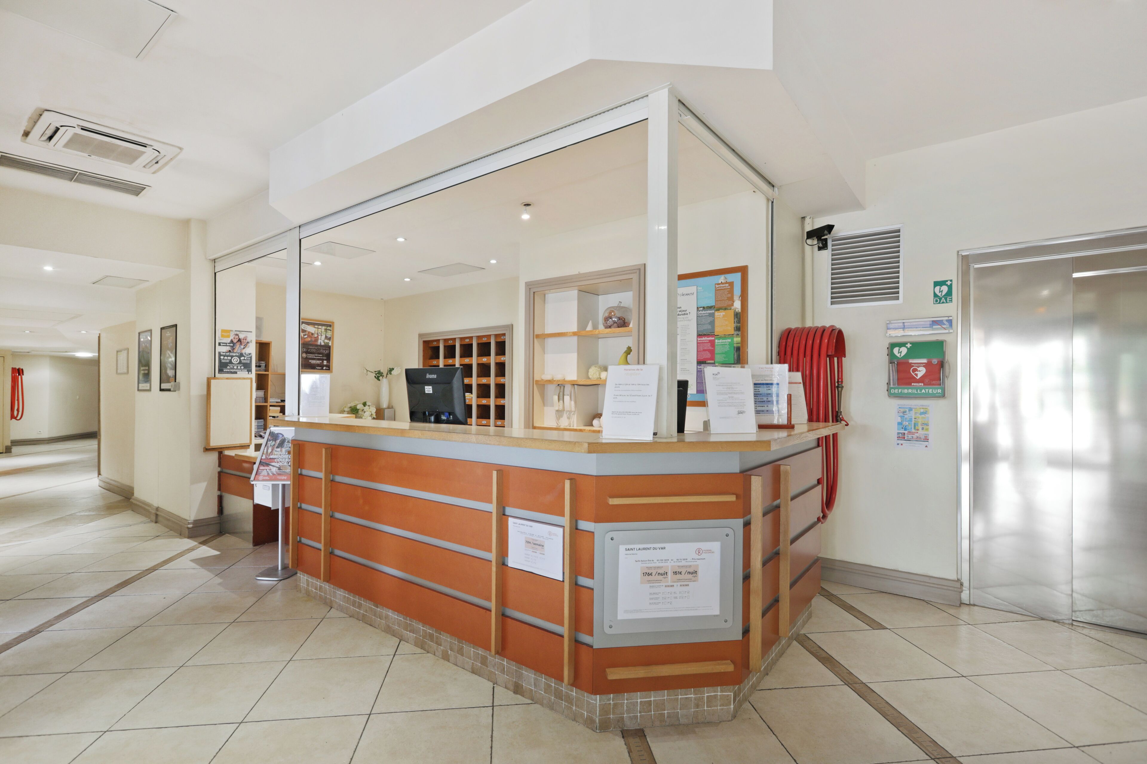Un área de recepción con mostrador, computadora y refrigerador.