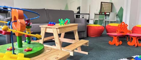 Un salon avec un canapé gris, une table en bois avec des jouets, un petit tabouret en bois et un espace de jeux coloré.