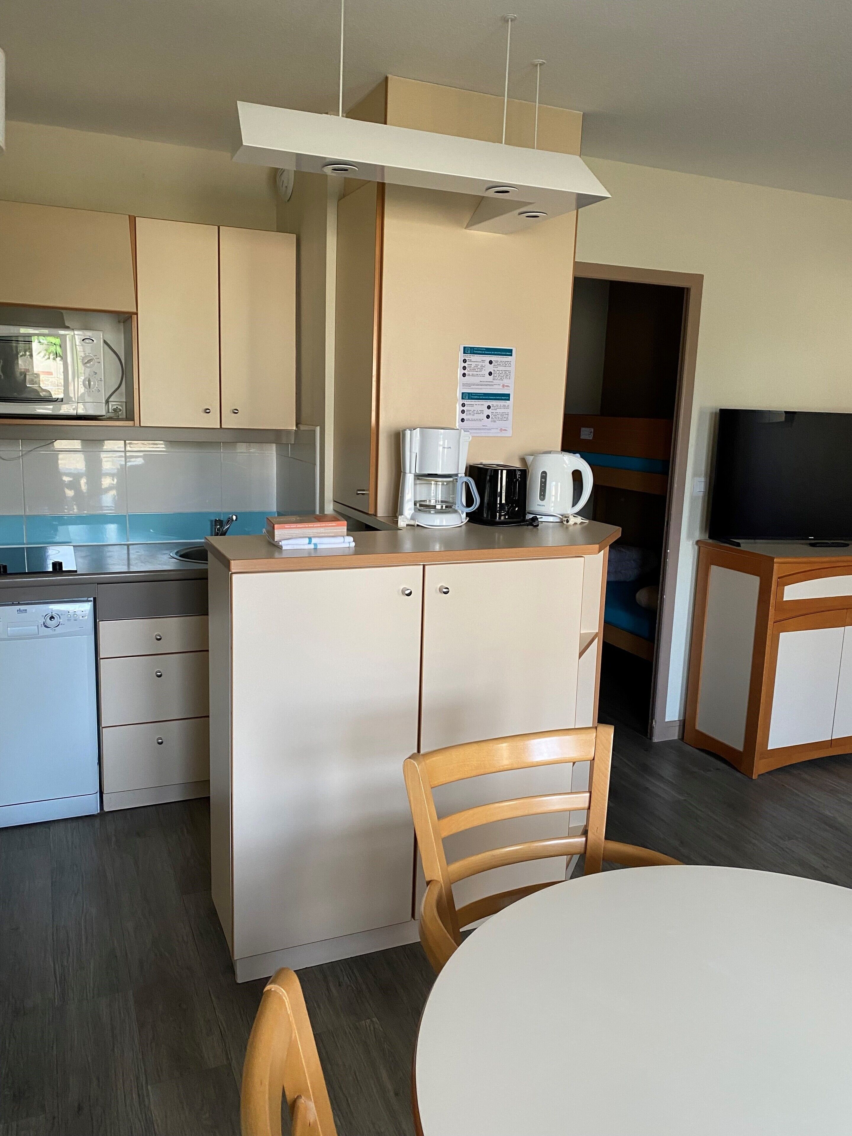 A compact kitchenette with a microwave, coffee maker, and kettle, a small dining table with chairs, and a television.