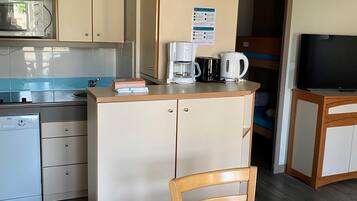 A compact kitchenette with a microwave, coffee maker, and kettle, a small dining table with chairs, and a television.