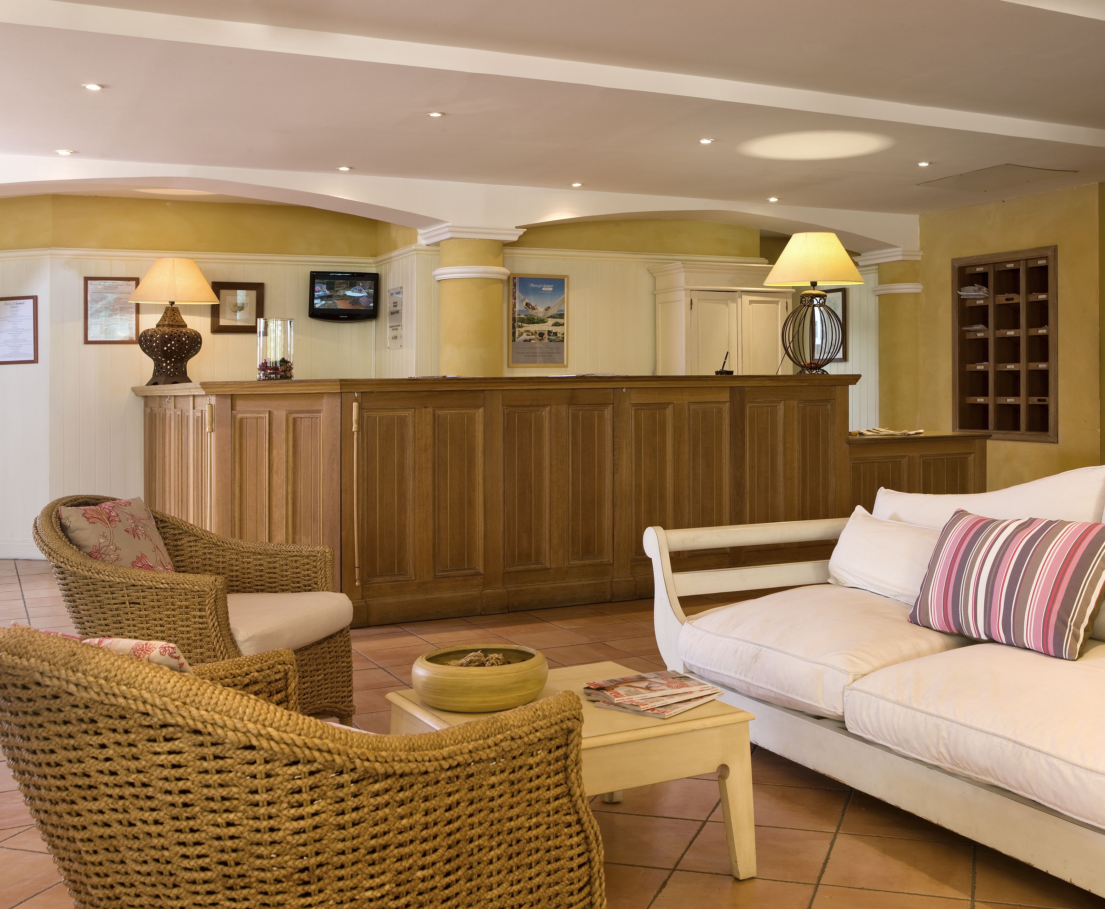 Un salón acogedor con muebles de mimbre, un sofá blanco y un mostrador de recepción de madera.