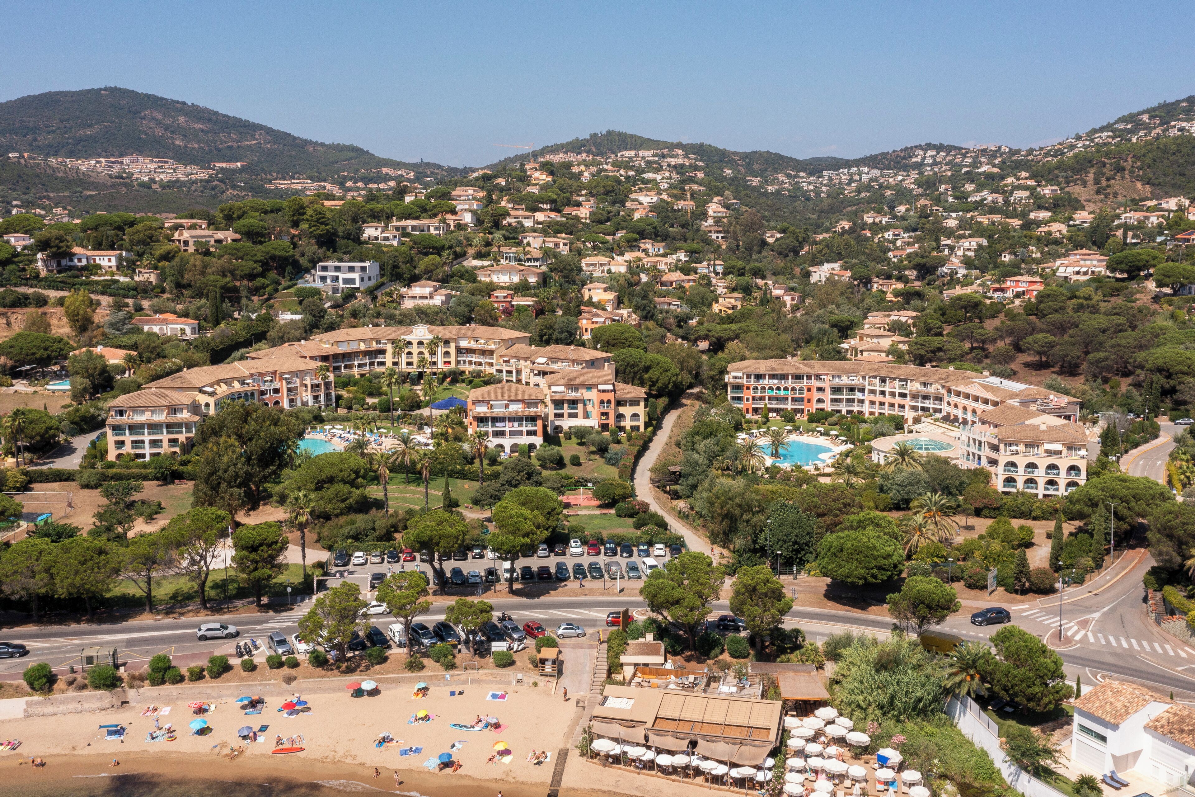 Un resort costero con varias edificaciones, una zona de playa con sombrillas y una piscina.