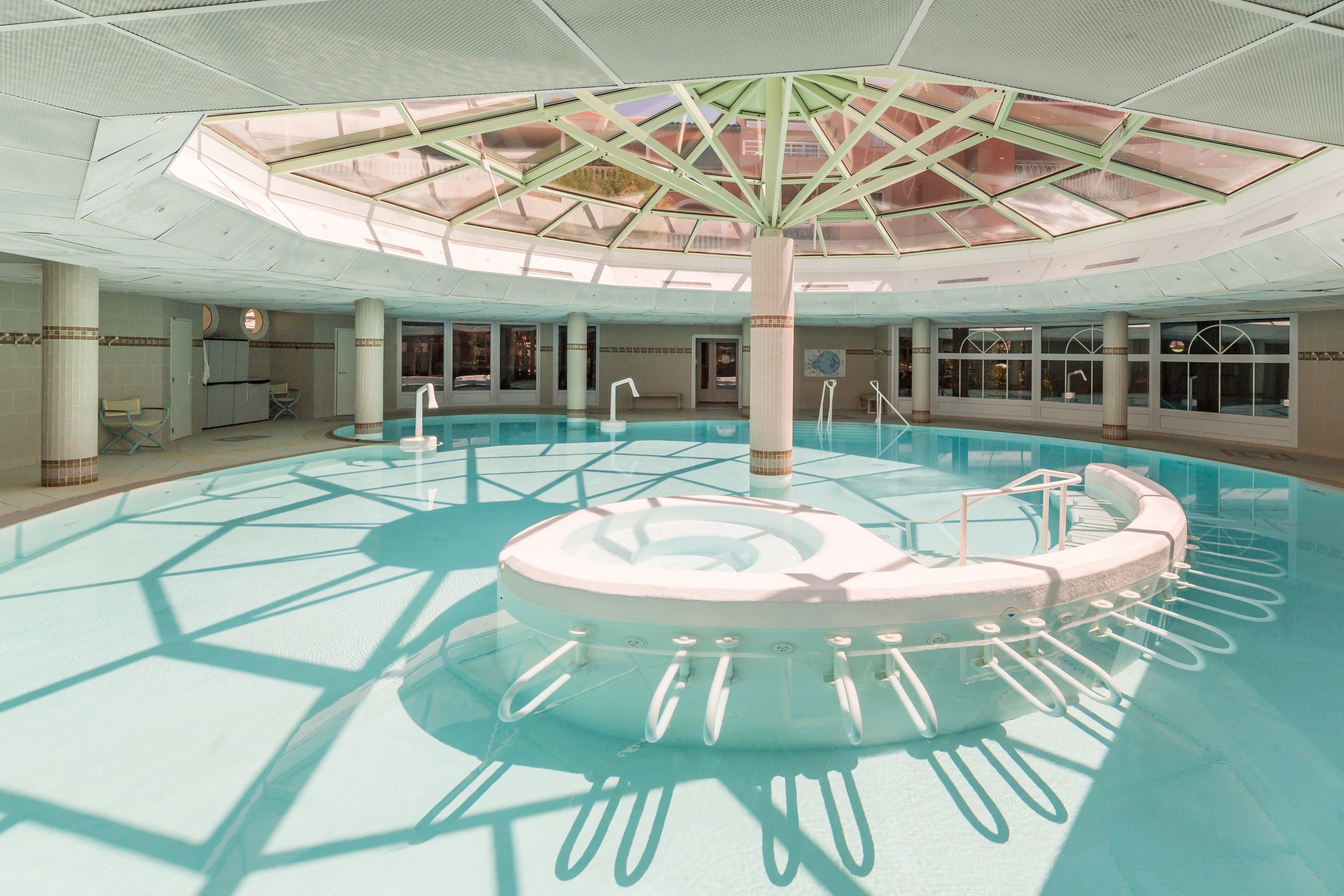 An indoor swimming pool with a central circular platform and a glass ceiling.