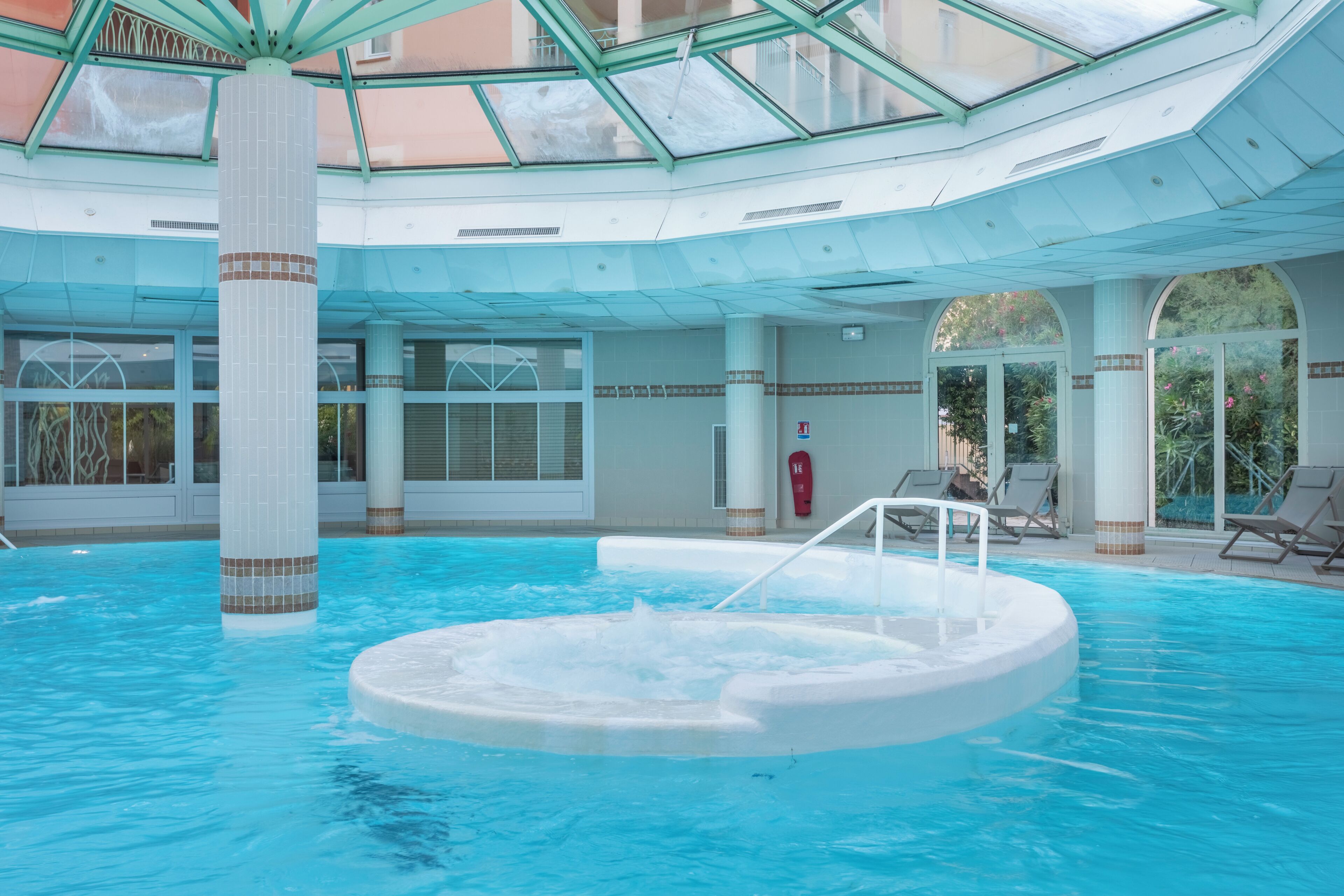 Piscina interna com hidromassagem, teto de vidro e espreguiçadeiras.