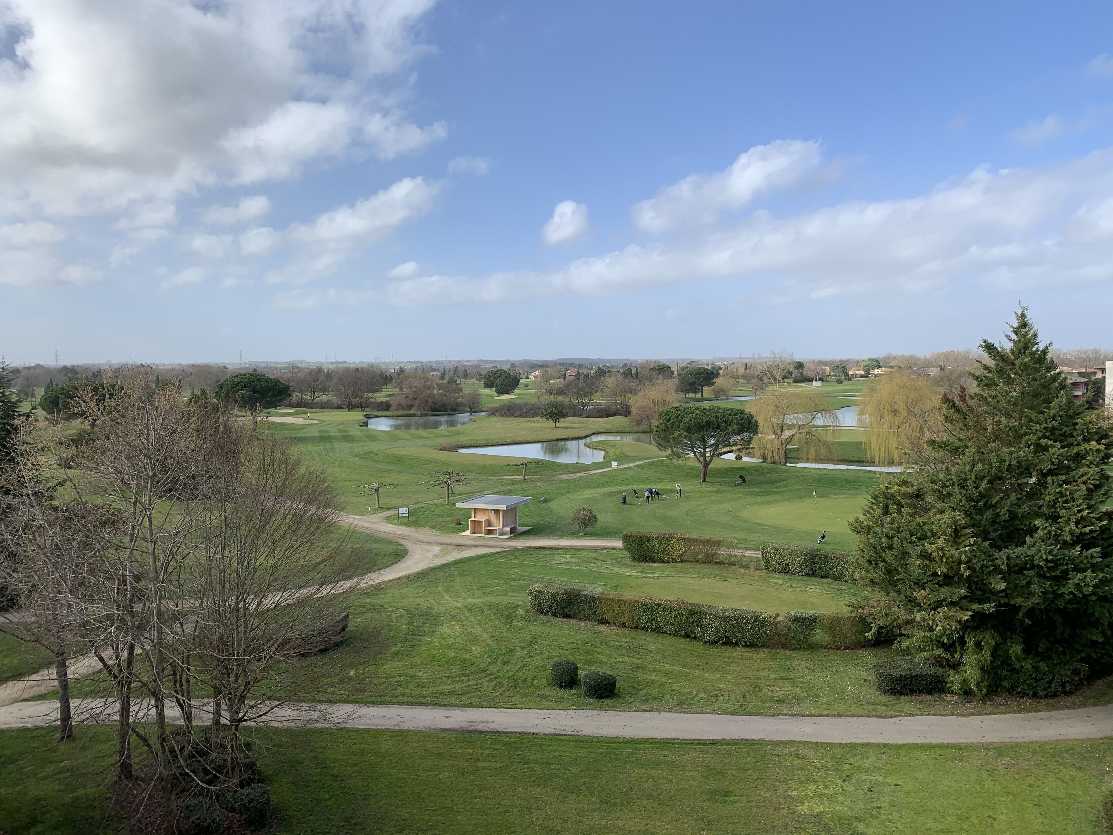 Un campo de golf con un estanque, árboles y un edificio pequeño.