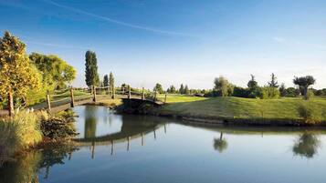 Una scena tranquilla lungo il fiume, con un ponte di legno, acqua calma e vegetazione rigogliosa.