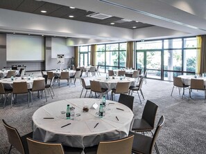 A conference room with round tables, chairs, and a projector screen. - Mercure Toulouse Aeroport Golf de Seilh (Seilh)