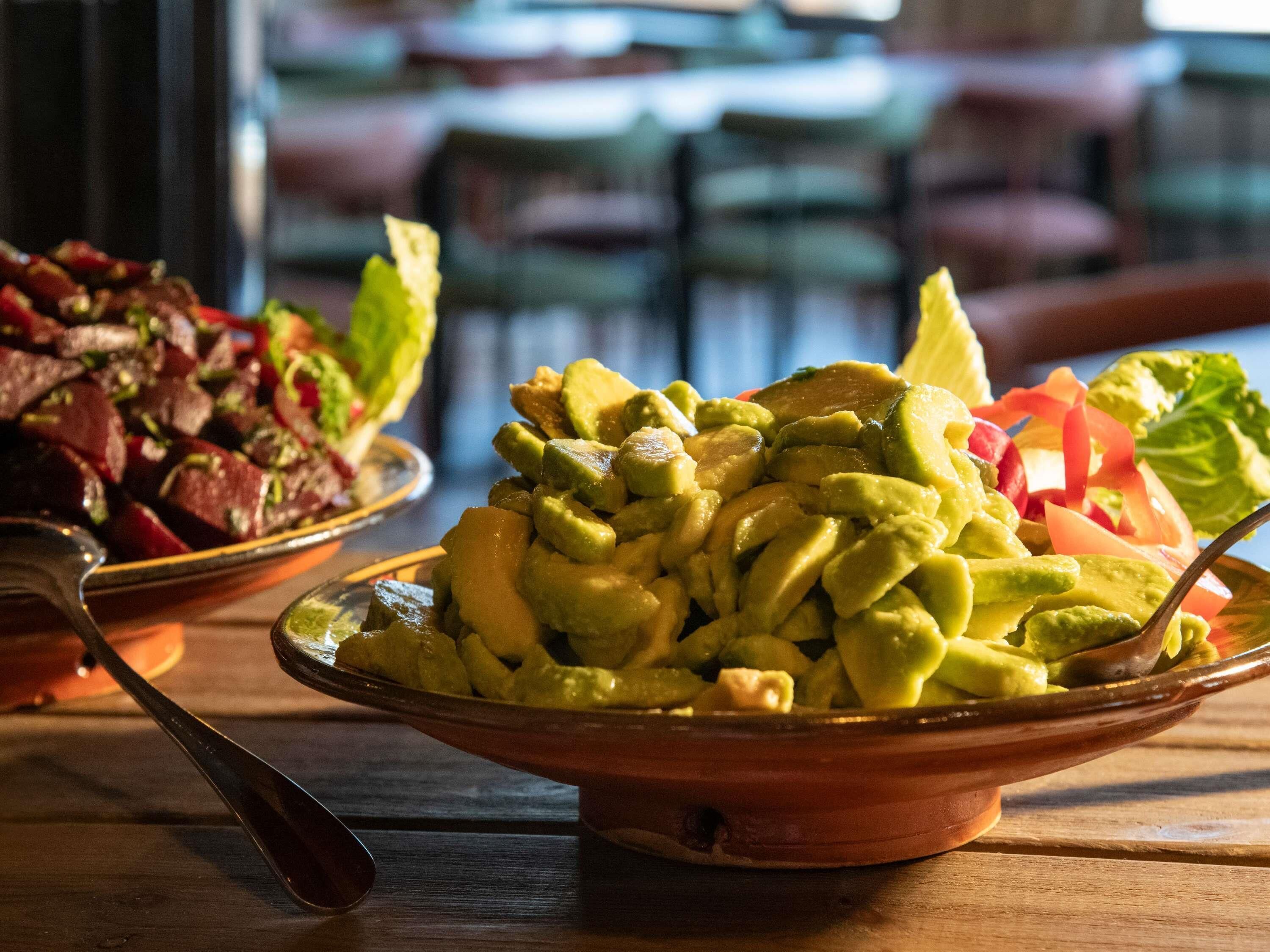 A table with bowls of food, including a dish with avocado and vegetables, and another with a meat dish.