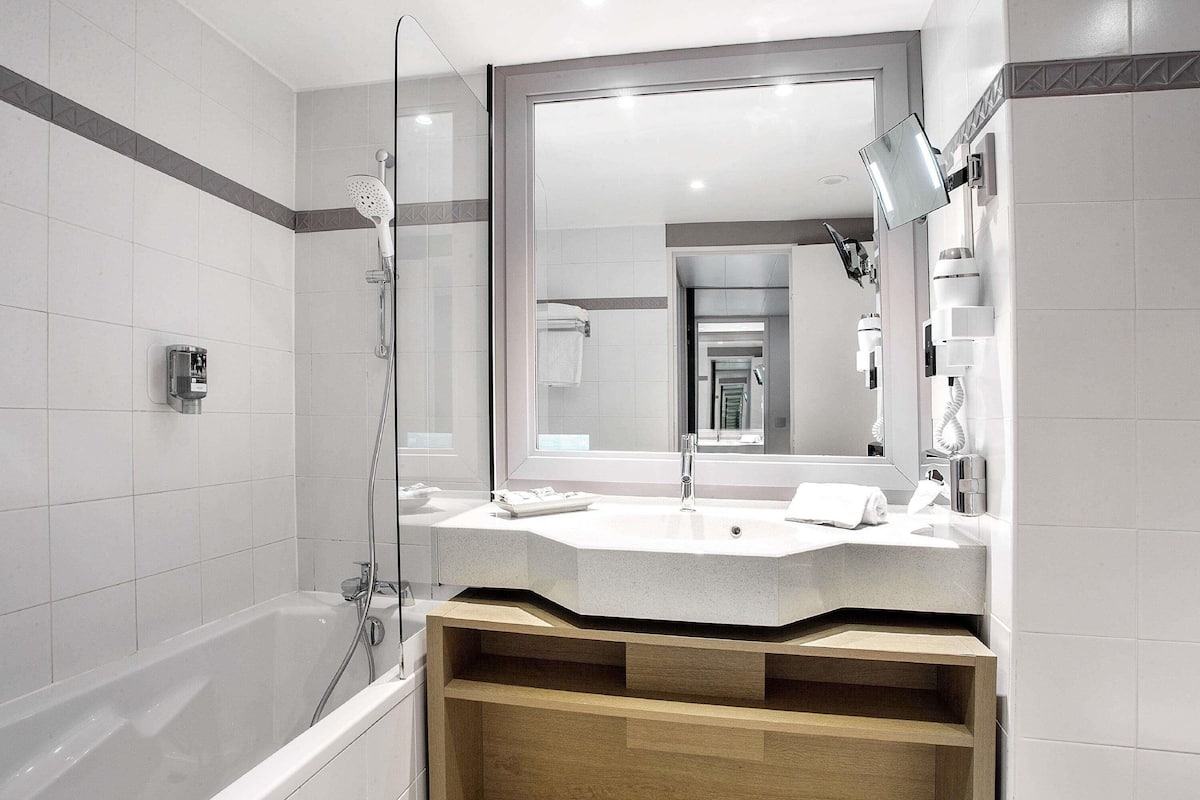A modern bathroom with a large mirror, a bathtub, and a vanity with a sink and towel.