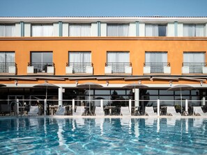 A hotel with a swimming pool, outdoor seating, and a bright orange facade. - Mercure Toulouse Aeroport Golf de Seilh (Seilh)