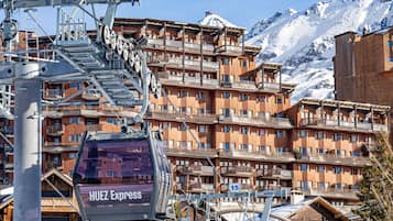A multi-story hotel with balconies, a ski lift, and snow-covered mountains in the background.