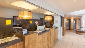 A reception desk with a wooden finish, a large vase, and a digital display. - Pierre & Vacances Residence L'Ours Blanc (Huez)
